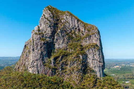 A close up shot of a volcanic plug. The stone structure is bare, except for a few trees that are able to grow on the stone peak. 
